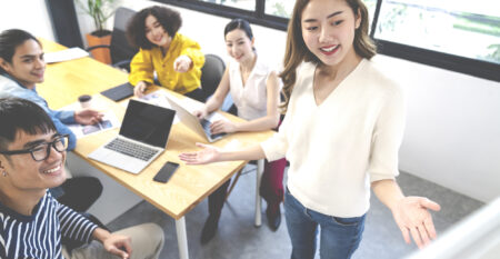 Young asian creative female leader standing making project presentation at office happy talking marketing idea with team. Casual people small business meeting workshop class with soft tone concept.